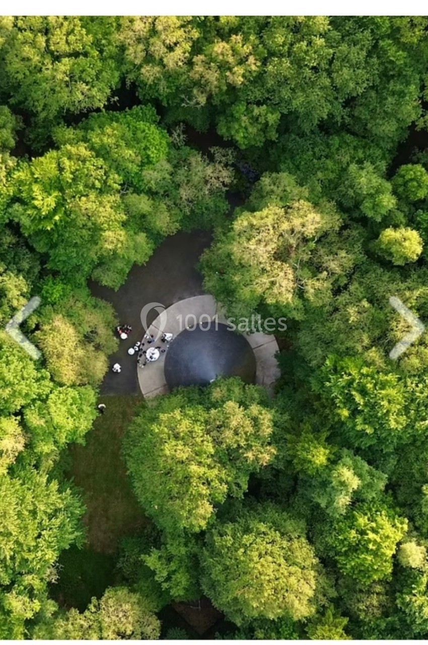 Vue aérienne d'une clairière entourée d'arbres, avec un petit espace circulaire et des personnes rassemblées.
