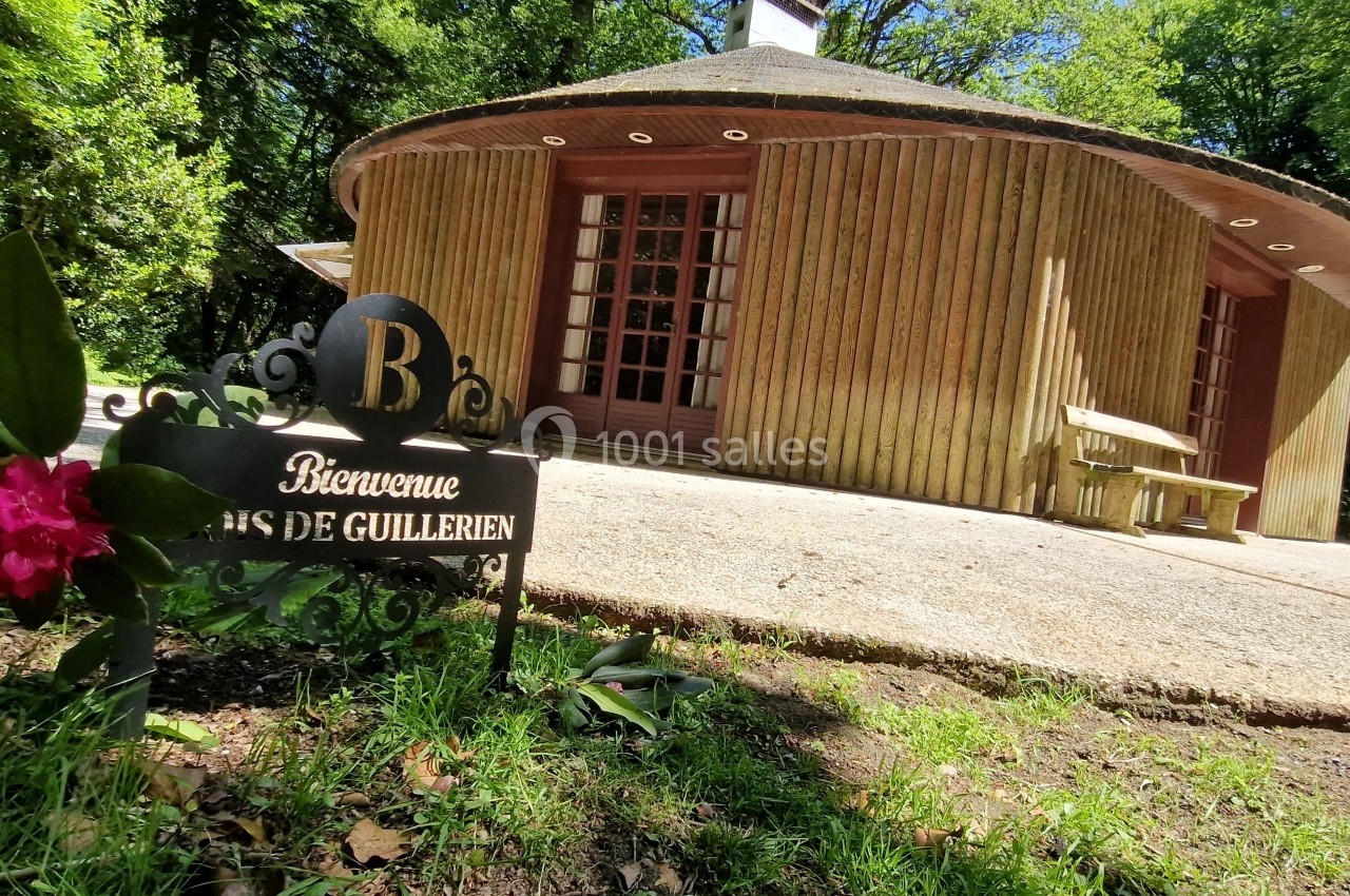 Bâtiment en bois entouré de verdure avec un panneau indiquant ’Bienvenue Bois de Guillerien’.