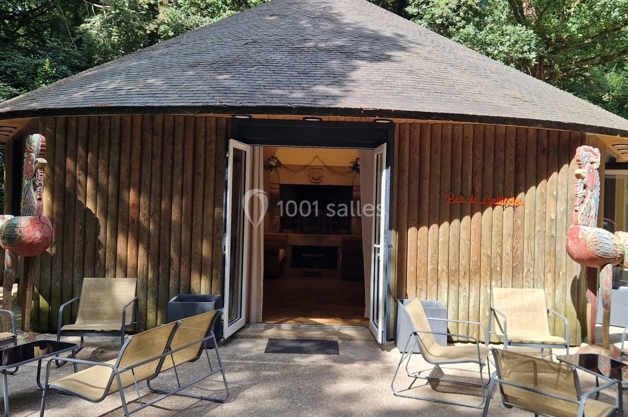 Entrée d'un bâtiment circulaire en bois avec des portes ouvertes, entourée de chaises et de sculptures colorées.