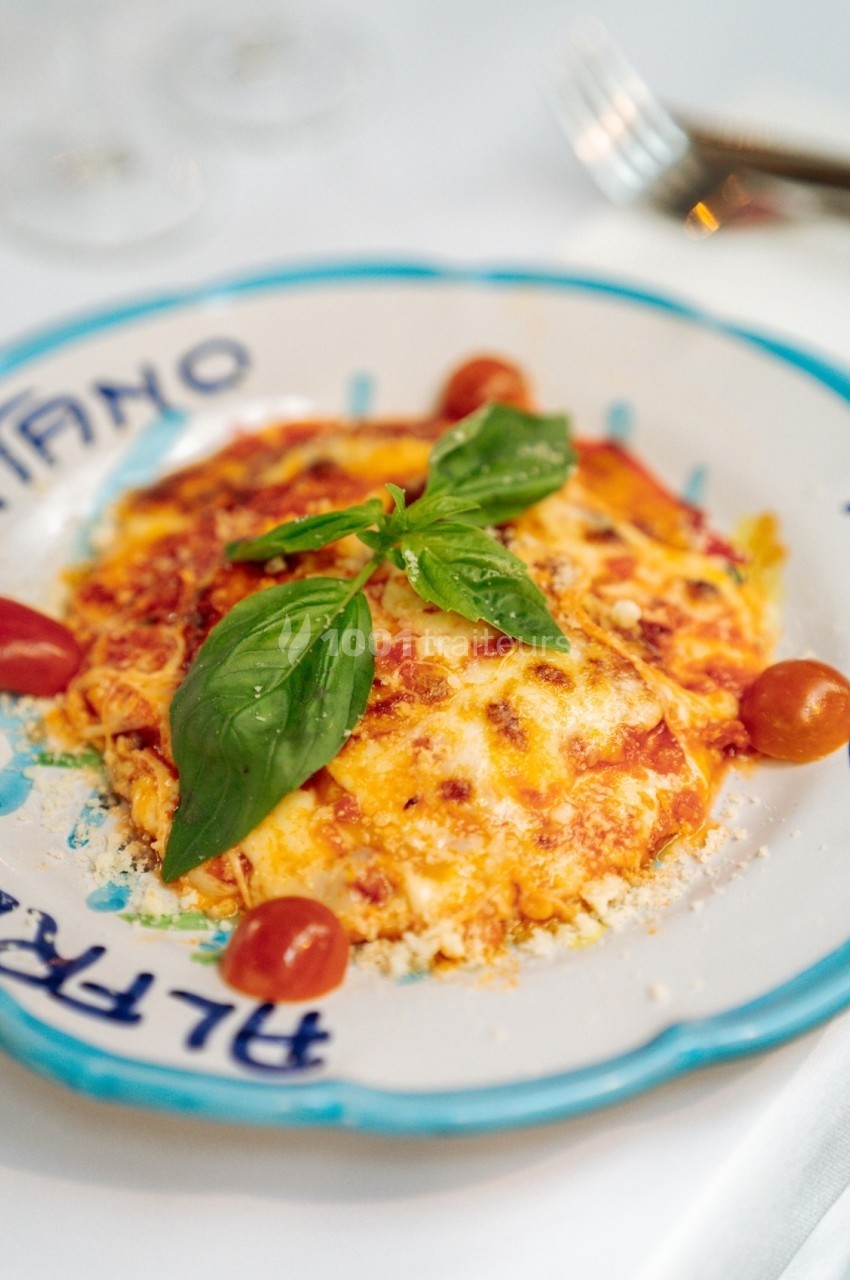 Assiette de lasagnes garnie de basilic frais et accompagnée de tomates cerises, servie sur une table dressée.