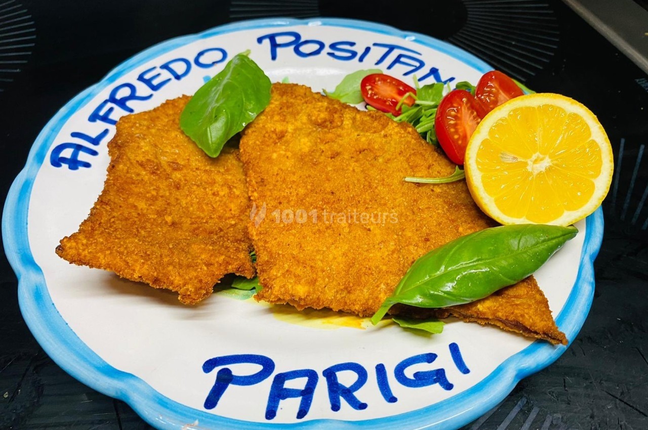 Assiette contenant deux escalopes panées, décorée de basilic, tomates cerises et un demi-citron.
