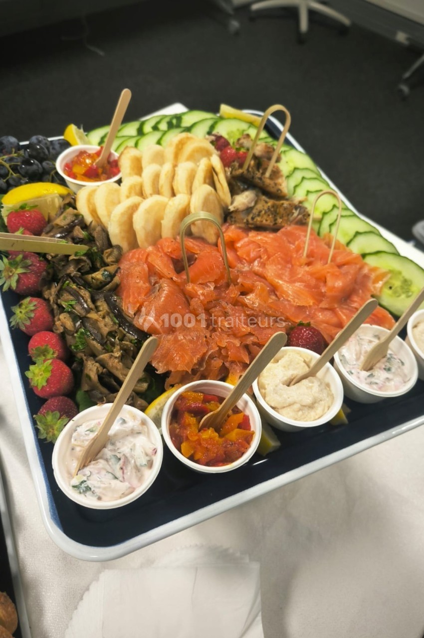Plateau de charcuterie avec saumon fumé, légumes frais, fruits, tartinades et biscuits apéritifs.
