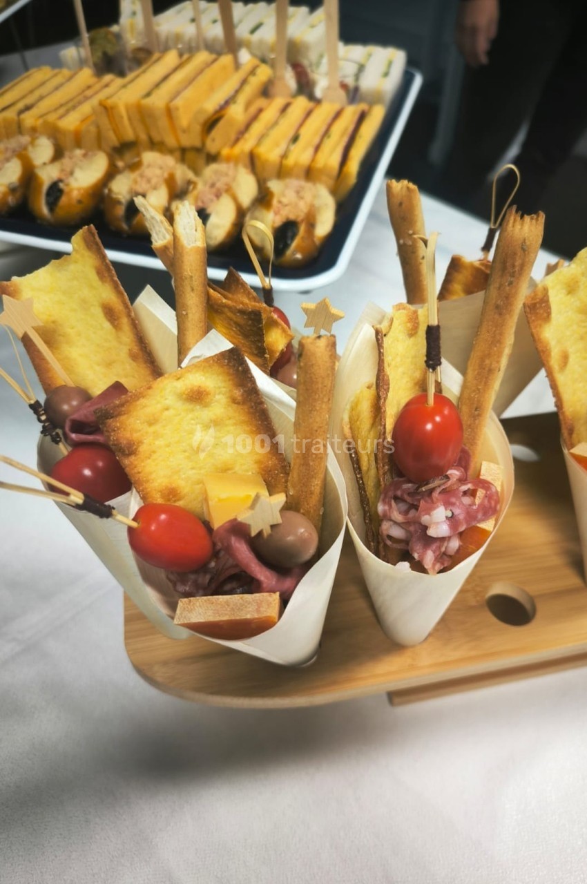 Cornets apéritifs garnis de gressins, tomates cerises, charcuterie et toasts, présentés sur un plateau en bois.