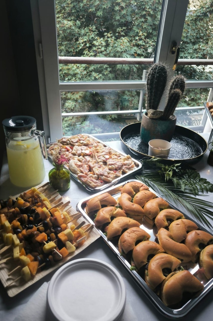 Buffet avec mini-sandwichs, brochettes de fruits, pizzas, carafe de citronnade et plantes en arrière-plan.