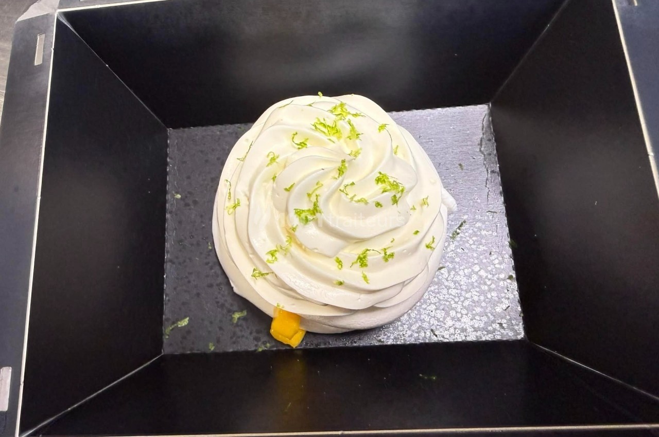 Meringue blanche décorée de zestes de citron vert, présentée dans un cadre noir rectangulaire.