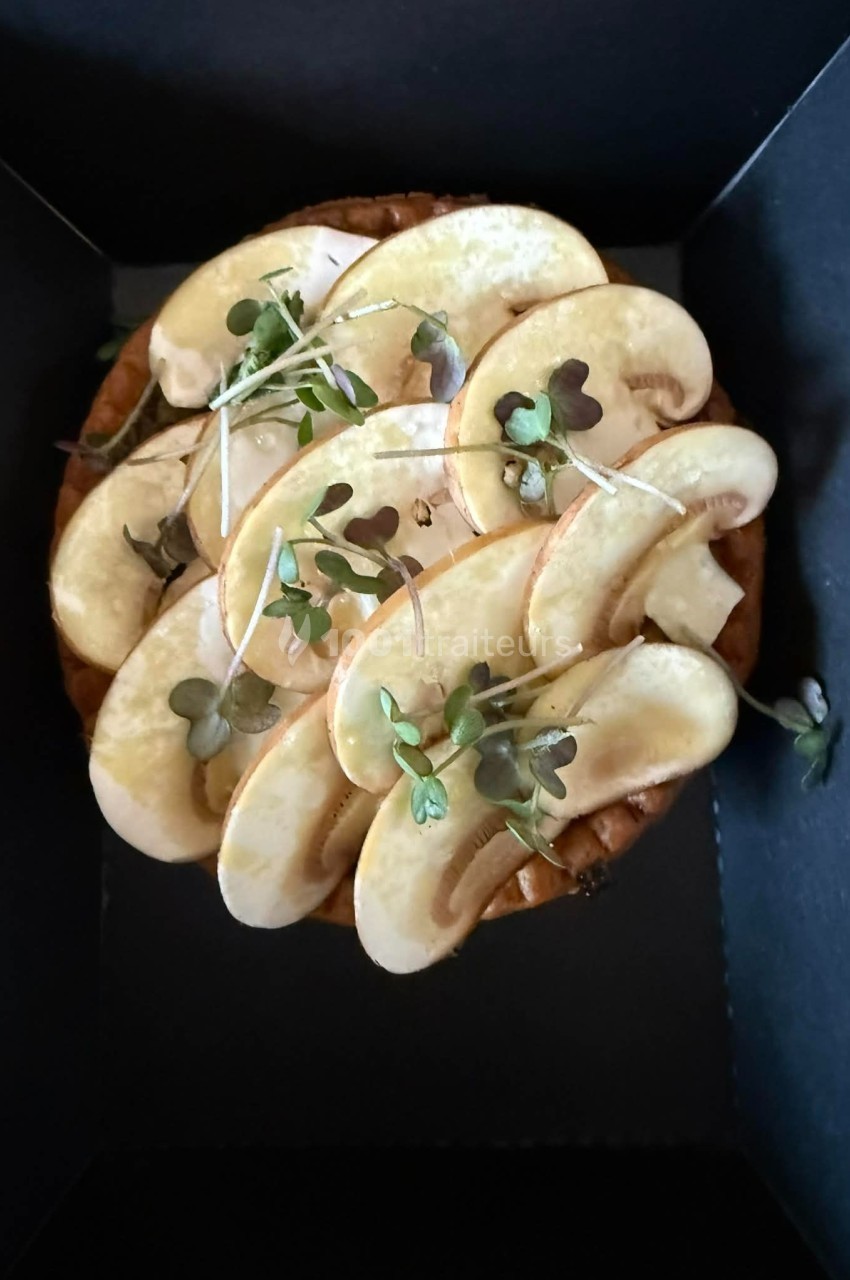 Tarte garnie de fines tranches de champignons frais et de jeunes pousses, présentée dans un emballage noir.