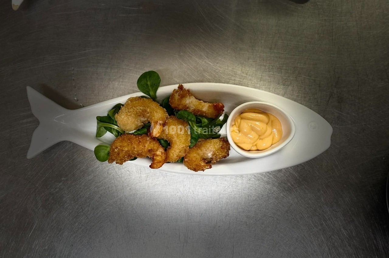 Assiette en forme de poisson contenant des beignets dorés, un lit de mâche et une sauce servie dans une coupelle.