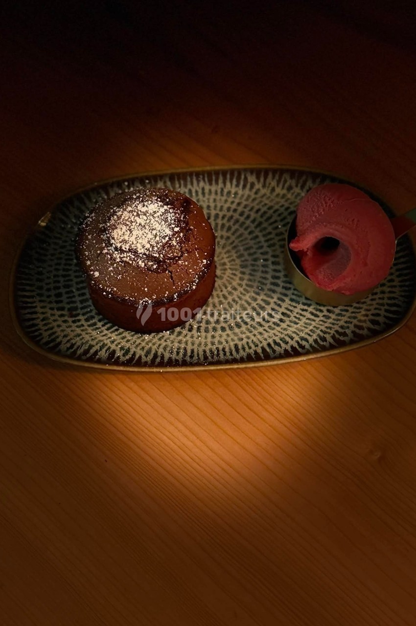 Dessert composé d'un fondant au chocolat saupoudré de sucre glace, accompagné d'une boule de glace rose sur une assiette.