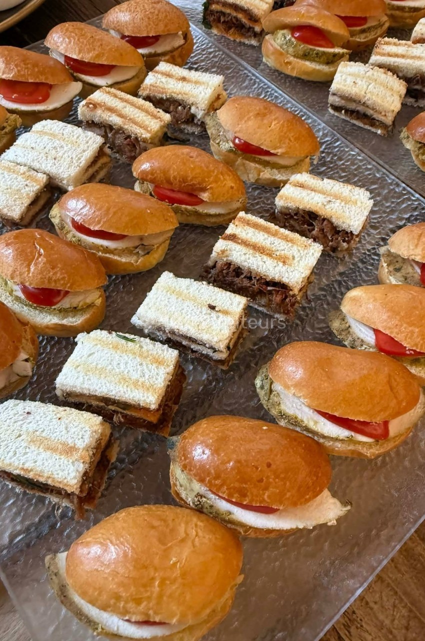 Plateau de mini-sandwichs variés comprenant des pains briochés garnis de tomates et des tranches de pain de mie.