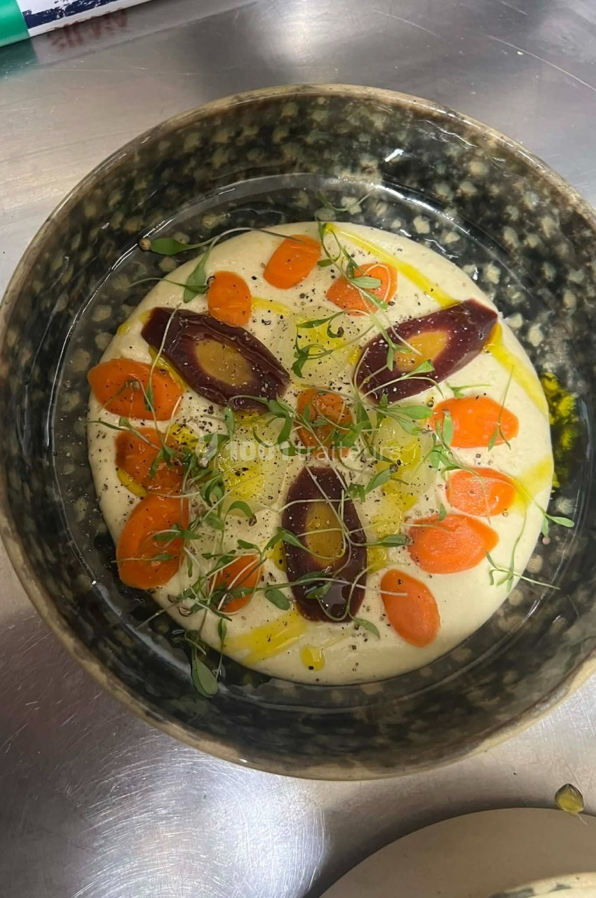 Bol contenant une purée crémeuse garnie de carottes, betteraves, herbes fraîches et filet d'huile.