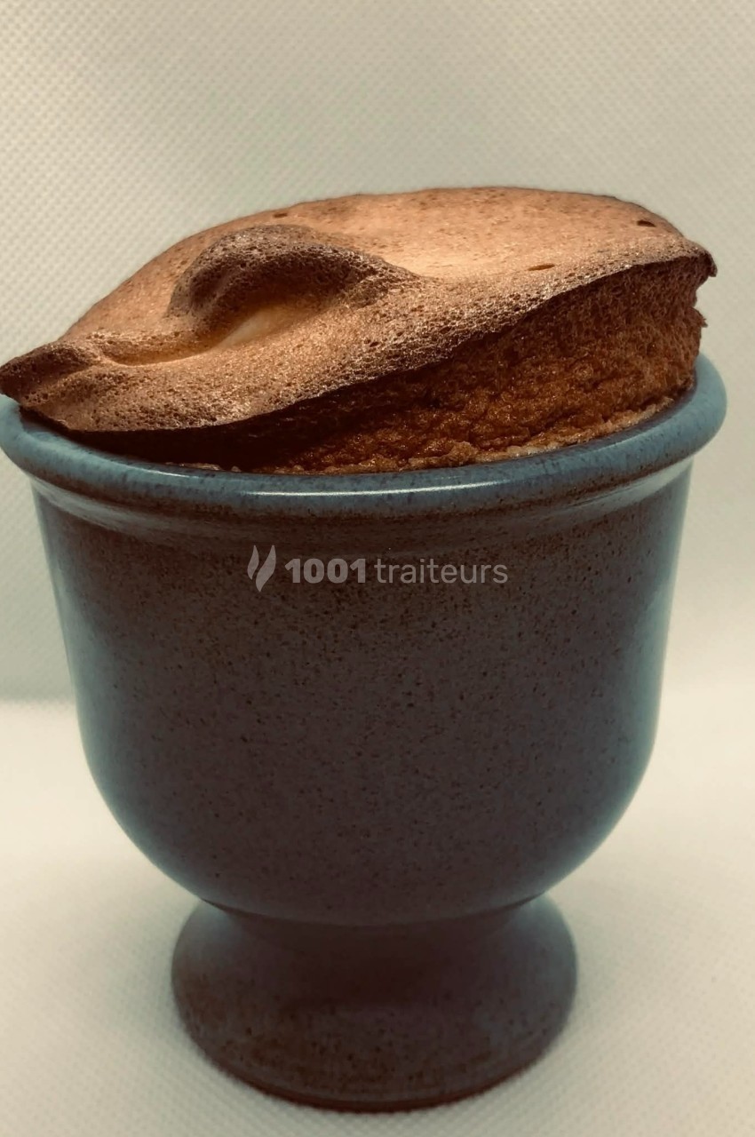 Soufflé doré et gonflé dans un ramequin en céramique bleue sur fond clair.