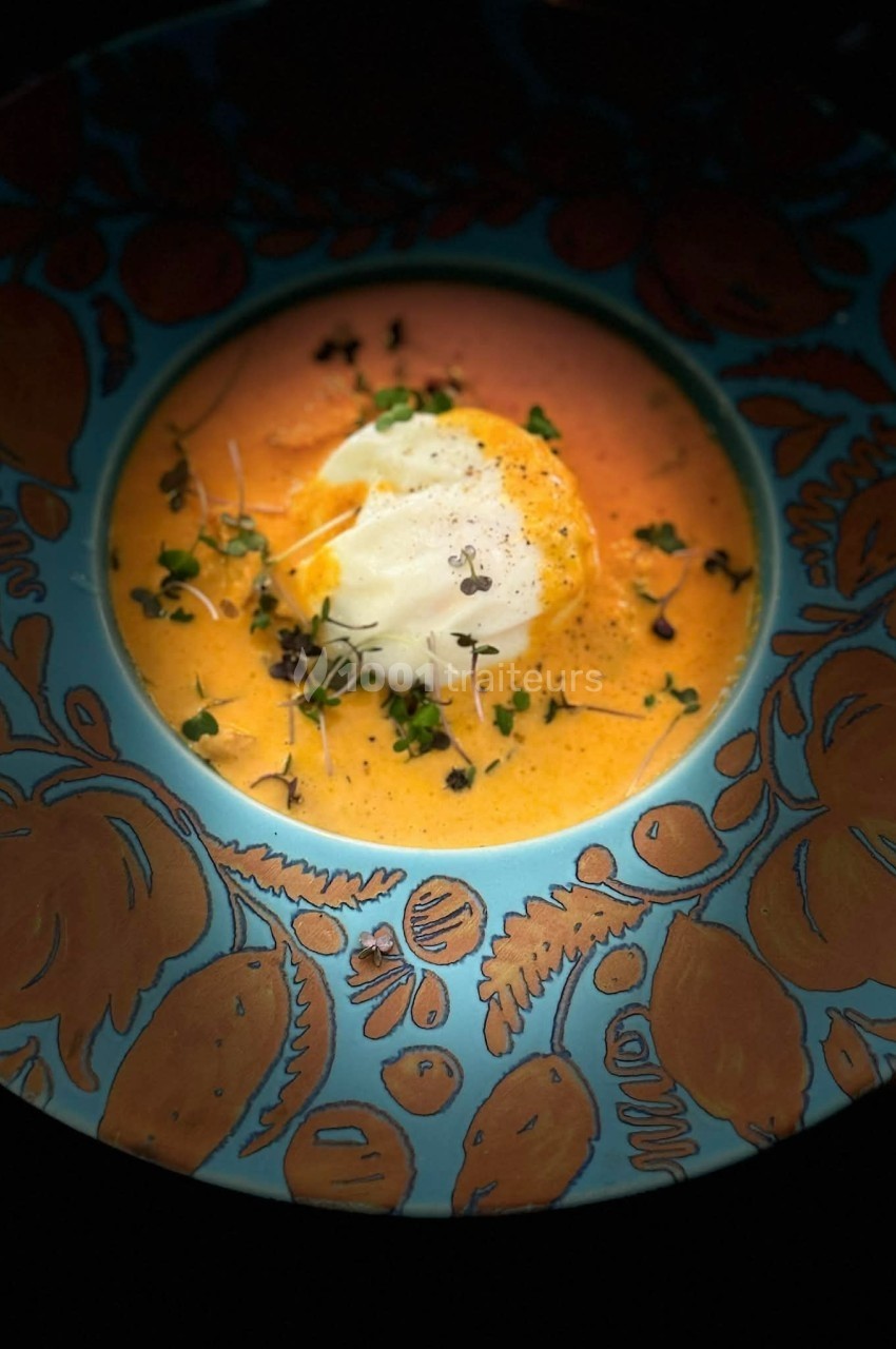Assiette colorée contenant une soupe orange garnie de crème, herbes fraîches et micro-pousses.