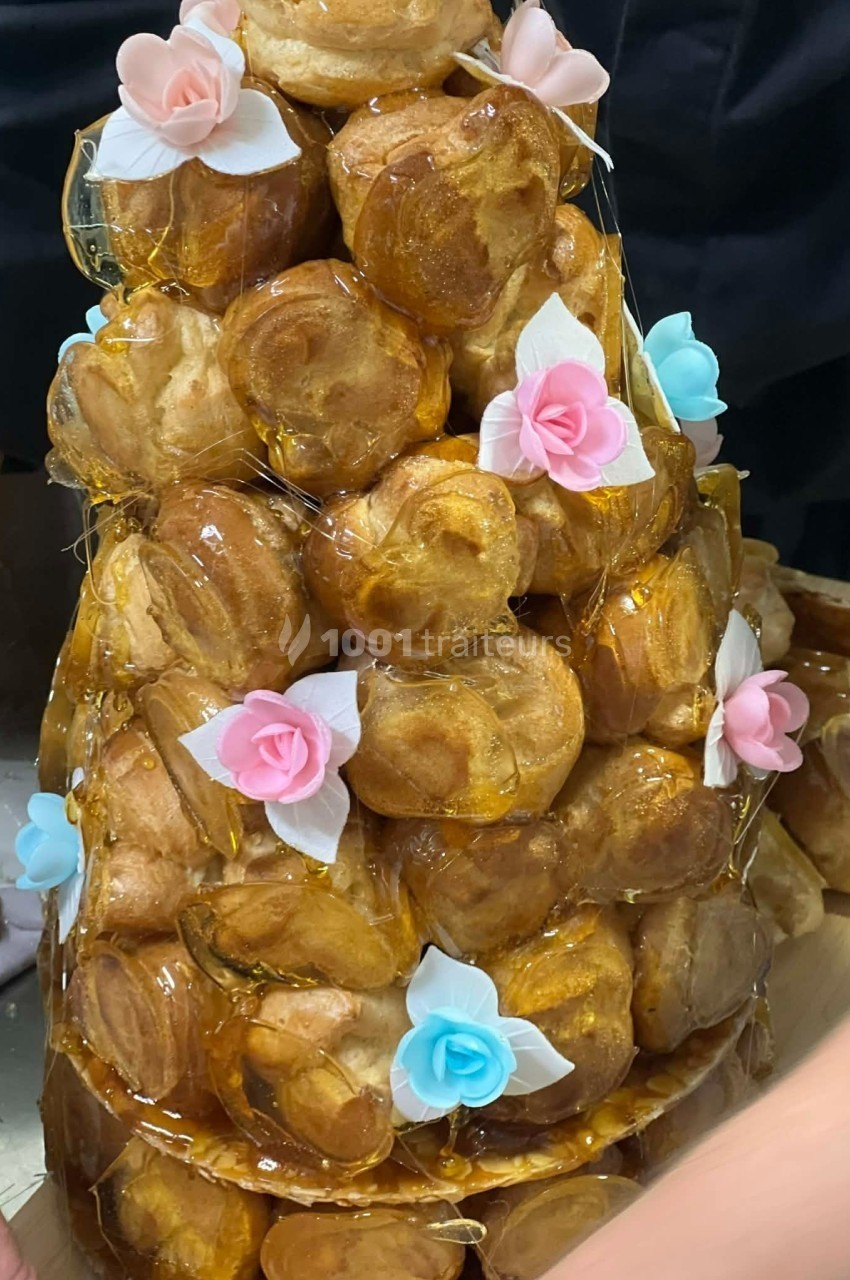Tour de choux garnis, assemblés avec du caramel et décorés de fleurs en sucre roses et bleues.