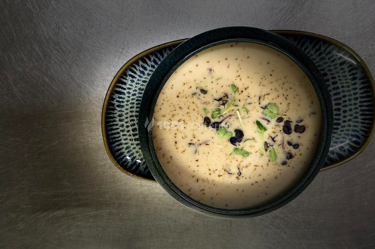 Bol de soupe crémeuse garnie de pousses vertes et de grains noirs, posé sur une surface métallique.
