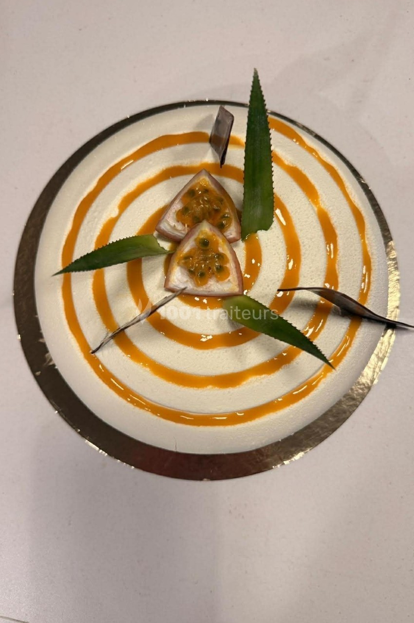 Gâteau rond décoré de spirales orange, morceaux de fruit de la passion et feuilles vertes sur le dessus.