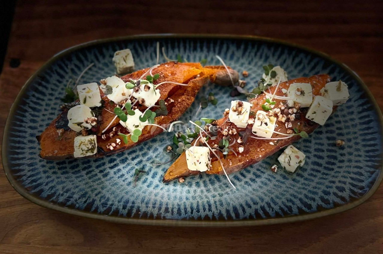 Patate douce rôtie garnie de fromage, graines, micro-pousses et herbes, servie sur une assiette bleue.