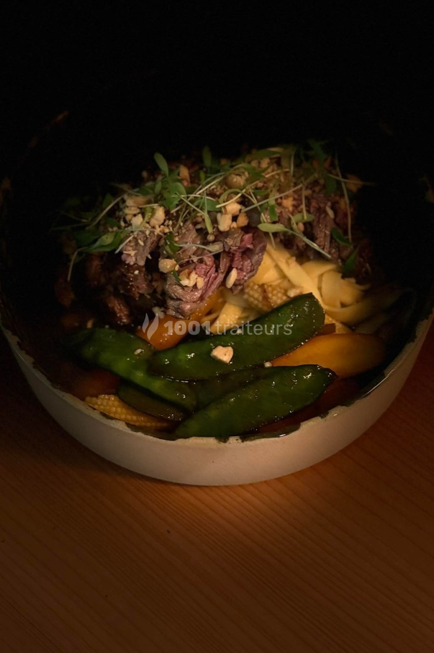 Bol de nouilles avec légumes croquants, viande effilochée, herbes fraîches et cacahuètes, éclairé dans une ambiance sombre.