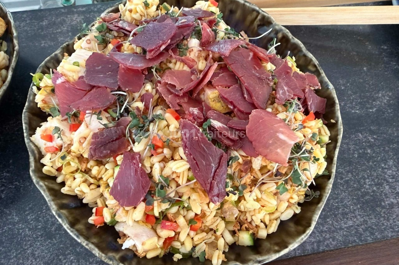 Assiette de salade de céréales garnie de tranches de viande séchée, légumes croquants et pousses fraîches.