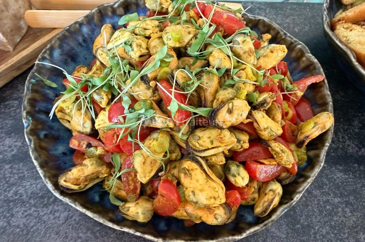 Assiette de moules marinées avec des morceaux de poivrons rouges et des pousses vertes, servie sur une table.