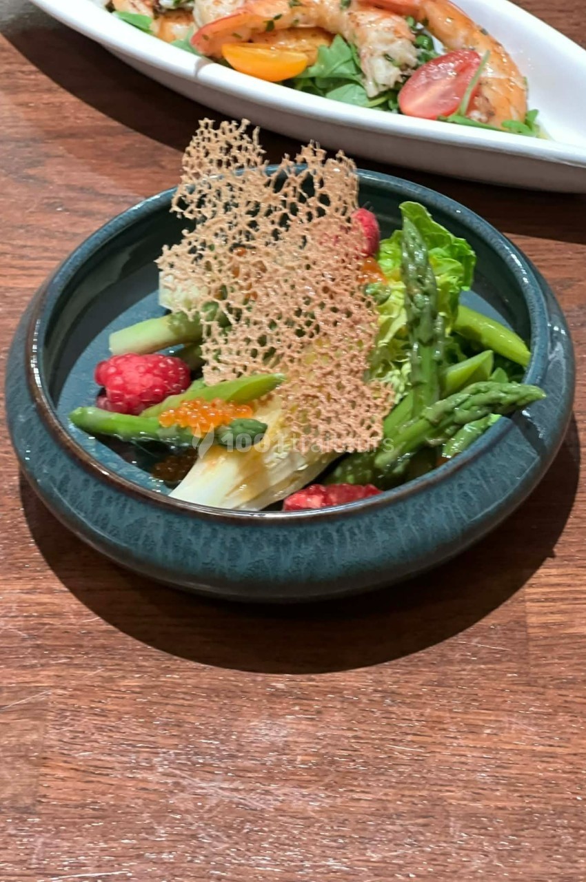Assiette garnie d'asperges, framboises, fenouil et tuile croustillante, présentée sur une table en bois.