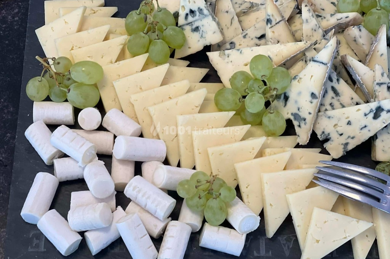 Plateau de fromages variés avec morceaux de chèvre, fromage à pâte dure, bleu et grappes de raisin vert.