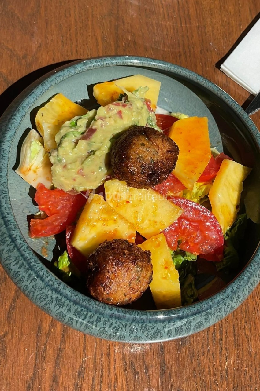 Assiette de salade colorée avec tomates, ananas, guacamole et boulettes végétariennes sur une table en bois.