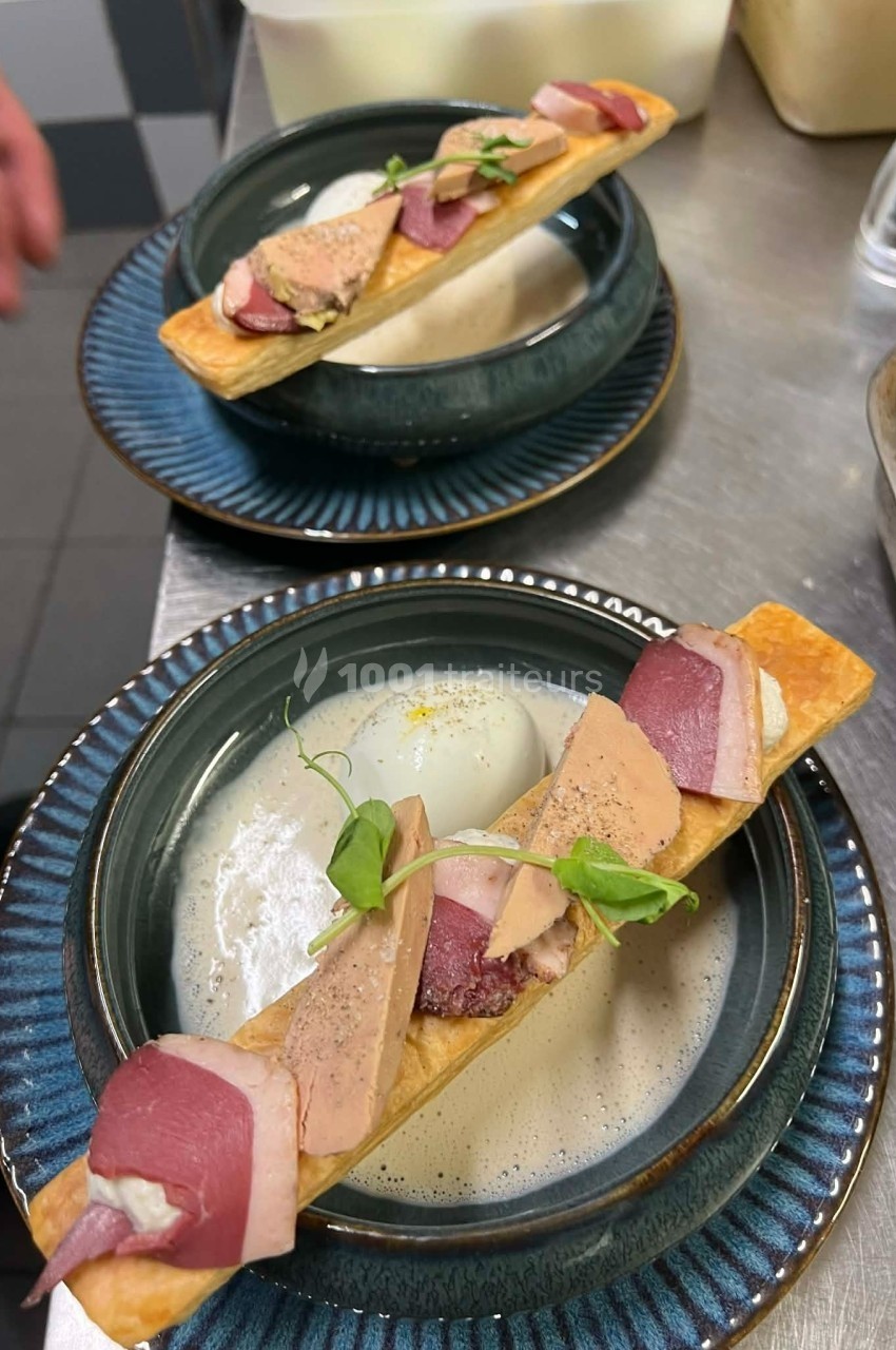 Deux assiettes contenant une préparation gastronomique avec magret de canard, mousse et herbes sur une pâte croustillante.