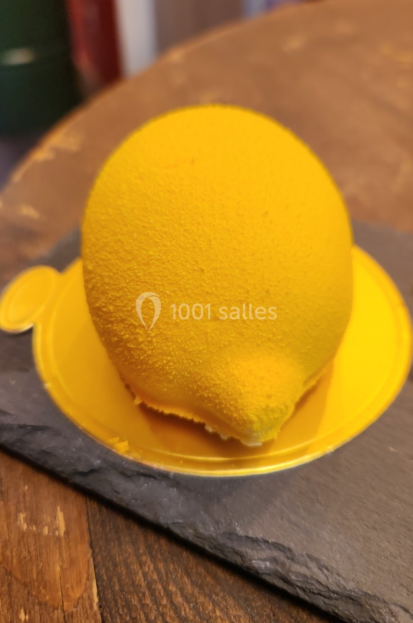 Dessert en forme de citron jaune texturé, posé sur une ardoise et un support en plastique jaune.