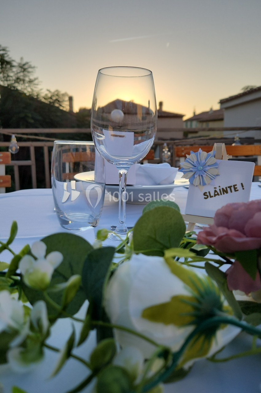 Verres et décorations florales sur une table dressée en extérieur au coucher du soleil.