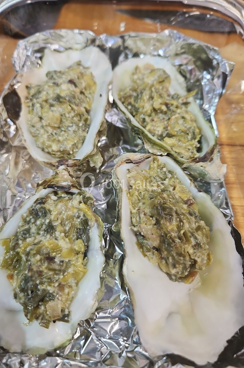 Quatre huîtres gratinées garnies d'un mélange crémeux aux légumes, présentées sur une feuille d'aluminium.