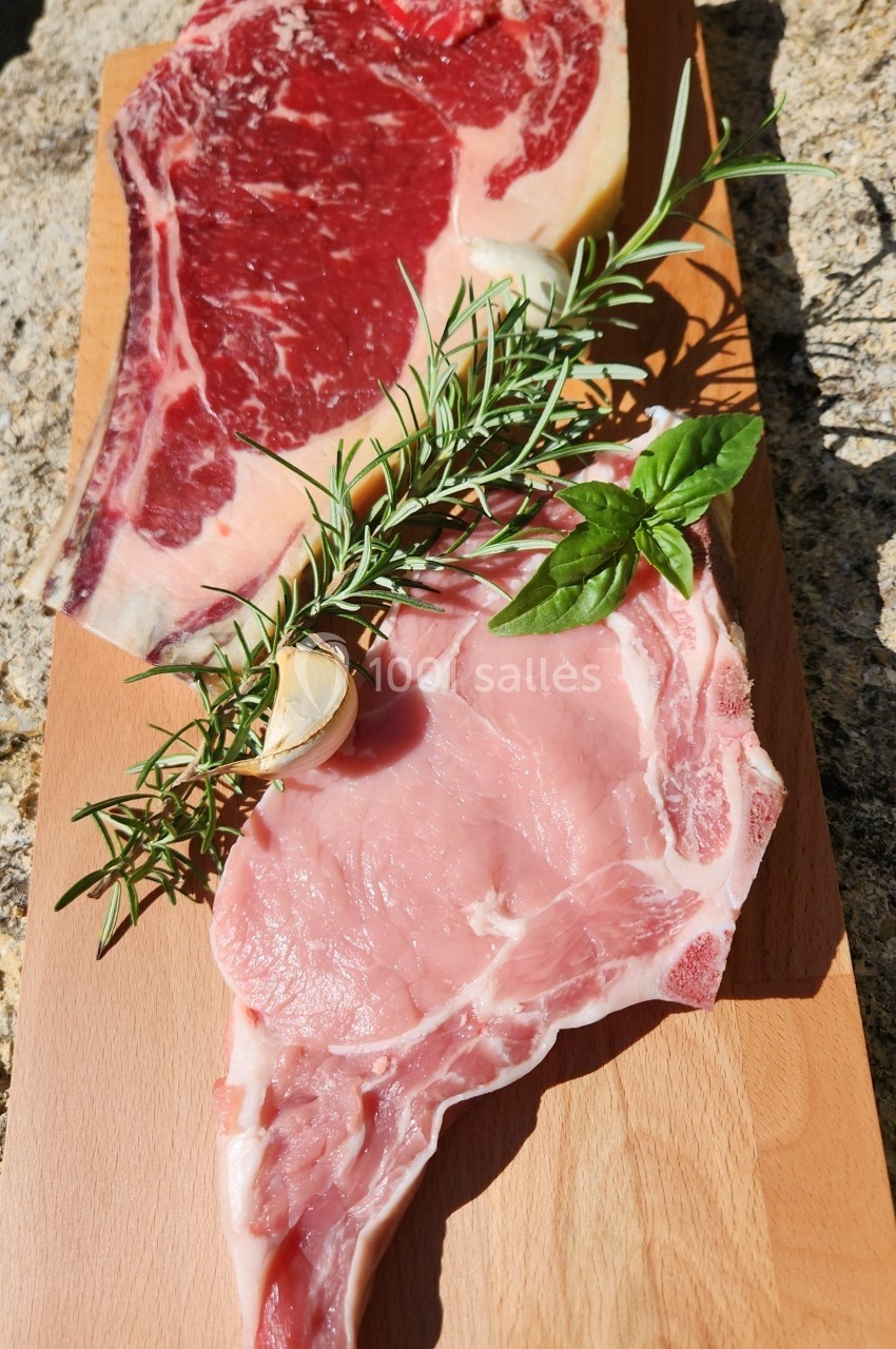 Deux morceaux de viande crue, l'un rouge et l'autre rose, posés sur une planche en bois avec des herbes aromatiques.