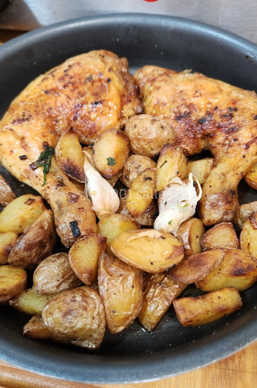 Poulet rôti avec des pommes de terre dorées et de l'ail dans une poêle noire.