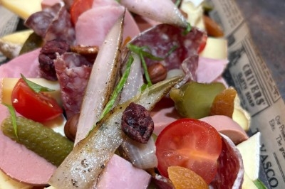 Plateau de charcuterie et fromages avec cornichons, tomates cerises, oignons marinés et fruits secs, présenté sur du papier…
