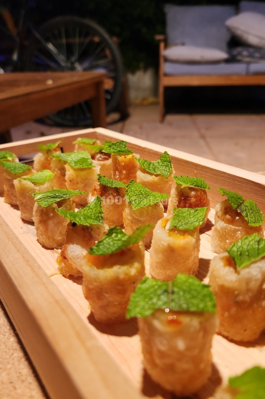Assortiment de bouchées croustillantes garnies, décorées de feuilles de menthe, présentées sur un plateau en bois.