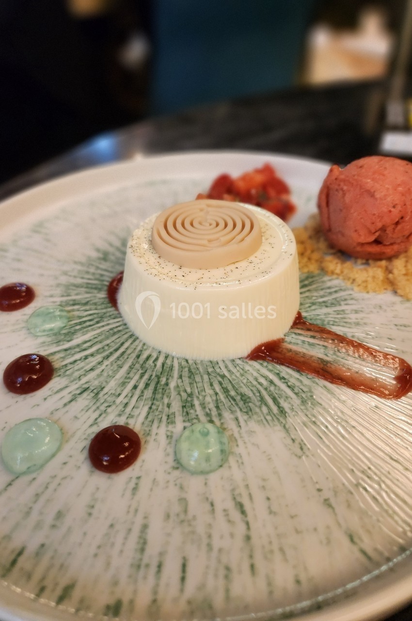 Dessert composé d'une panna cotta décorée, d'une boule de glace rose, de coulis et de touches de crème colorée.