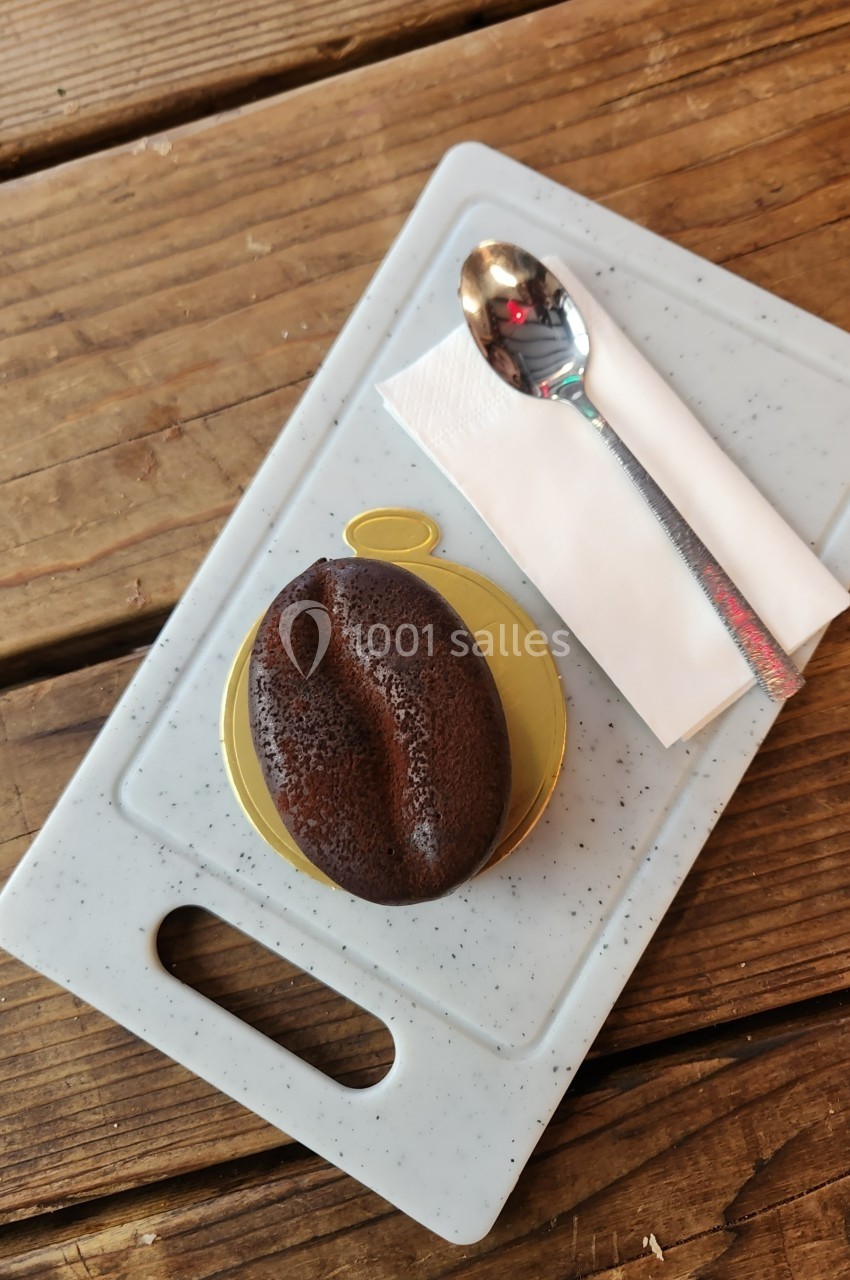 Un dessert en forme de grain de café sur une assiette blanche, accompagné d'une cuillère et d'une serviette.