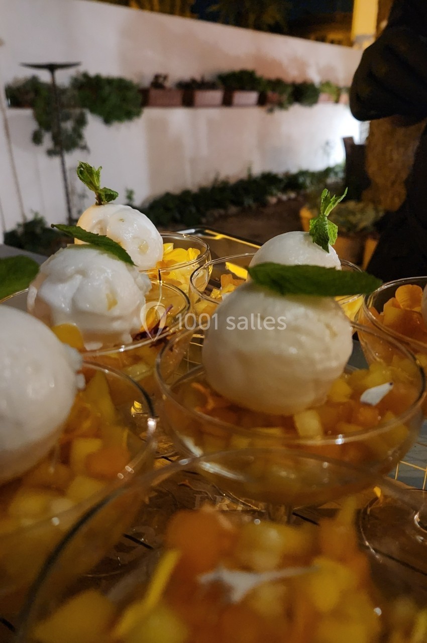 Coupes de glace vanille garnies de dés de fruits frais et de feuilles de menthe, présentées sur une table en extérieur.