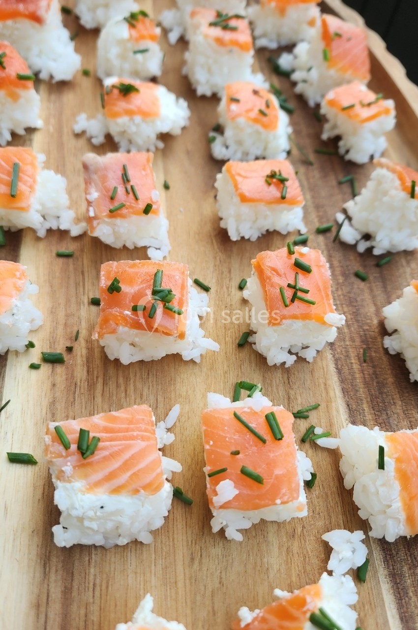 Sushis de saumon et riz disposés sur un plateau en bois, garnis de brins de ciboulette.
