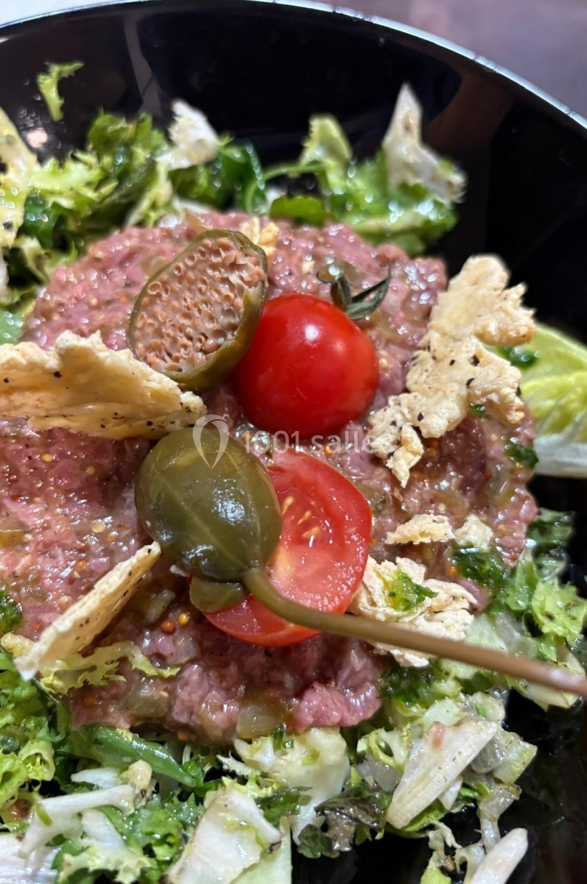 Assiette de tartare de viande avec tomates cerises, câpres, crackers et salade verte.