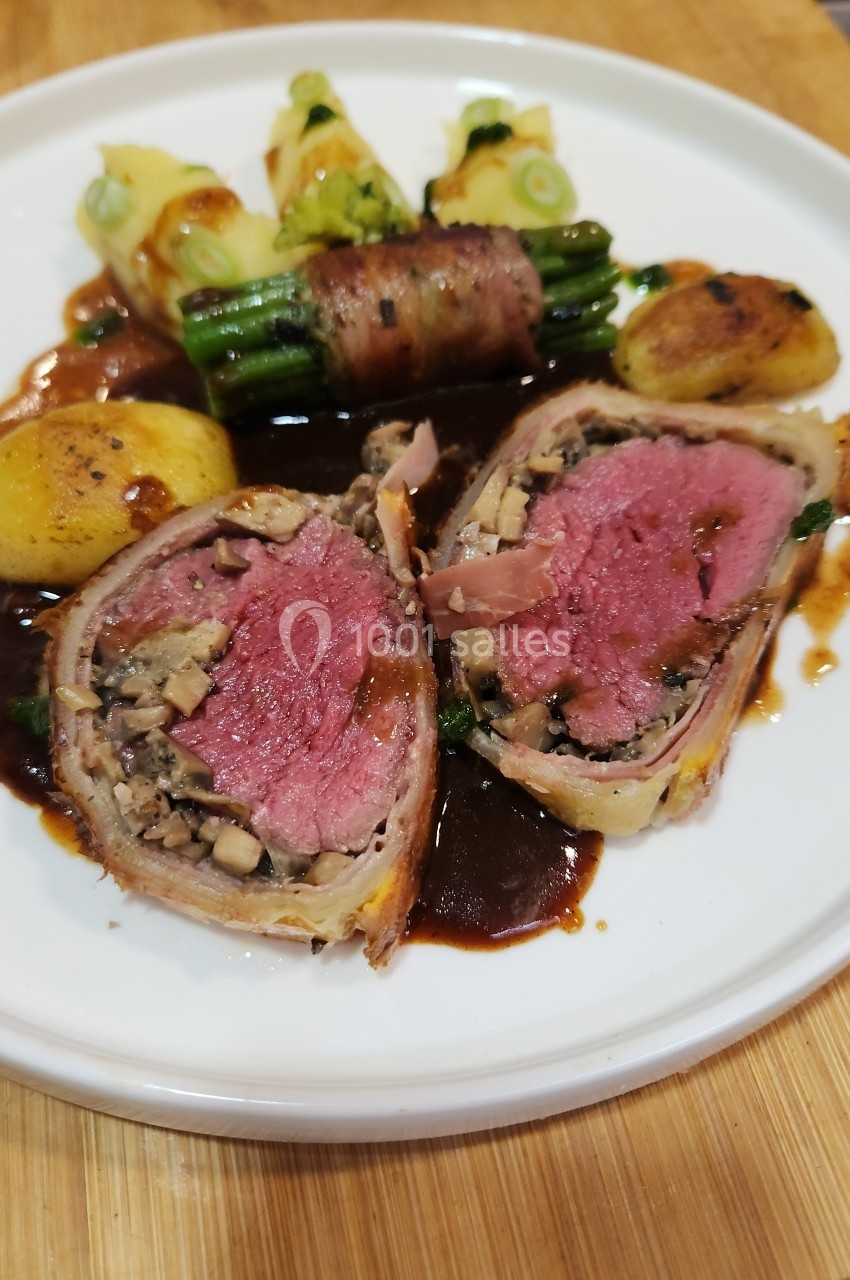 Plat de bœuf Wellington tranché, accompagné de légumes verts, pommes de terre rôties et sauce brune sur une assiette blanche.