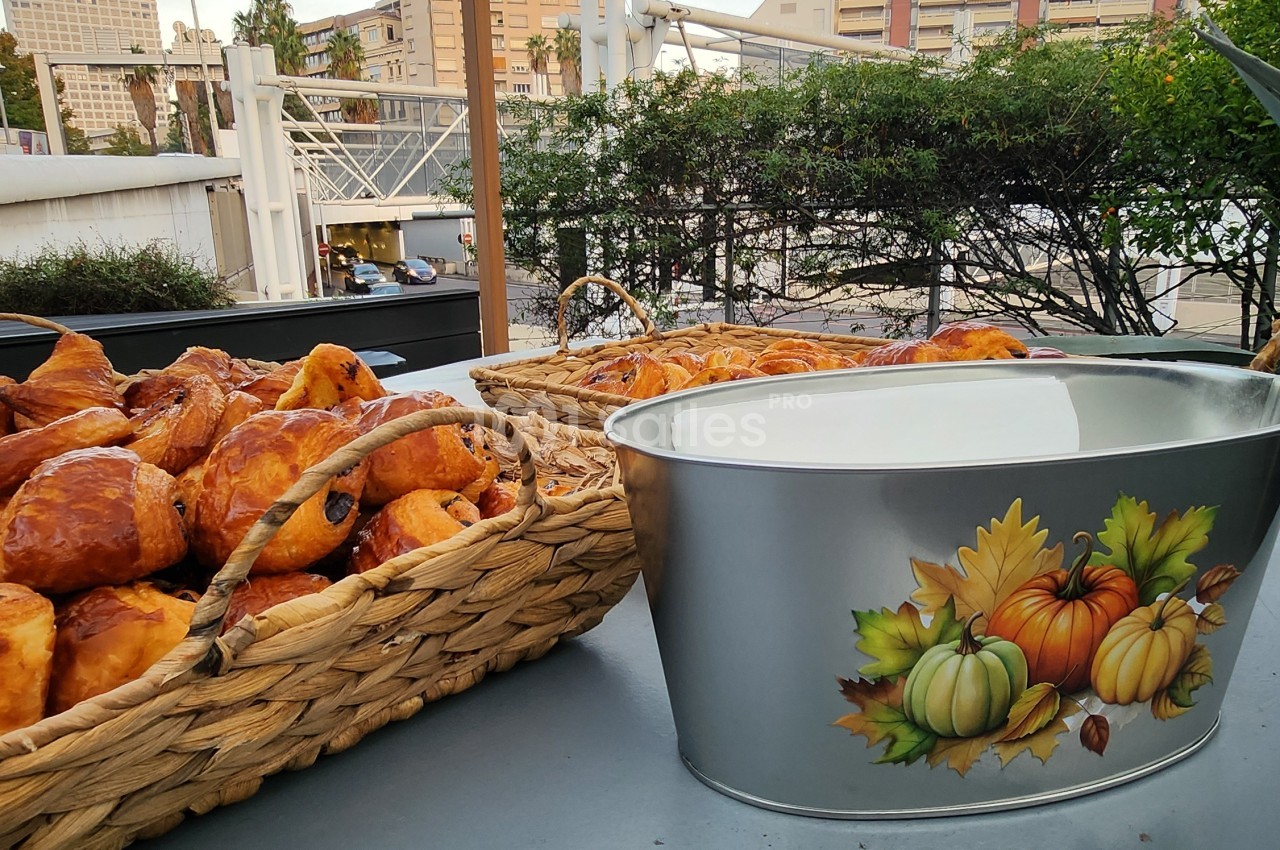 Paniers en osier remplis de viennoiseries dorées et seau métallique à motifs automnaux sur une table en terrasse extérieure.