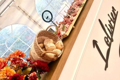 Illustration de deux oliviers entourant des tables et chaises disposées en extérieur, décorées de guirlandes lumineuses.