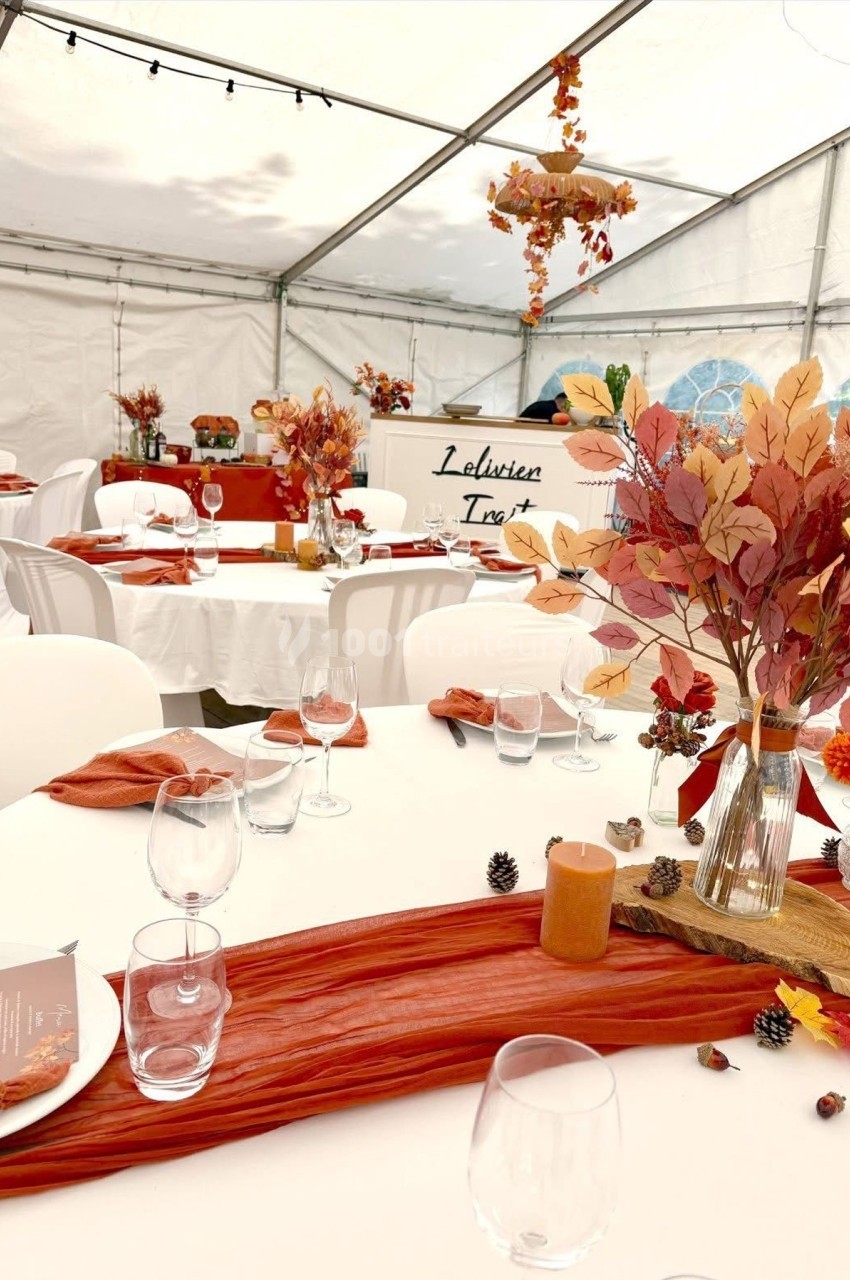 Table décorée dans une tente blanche, ornée de feuilles d'automne, nappes rouges et bougies pour une ambiance chaleureuse.
