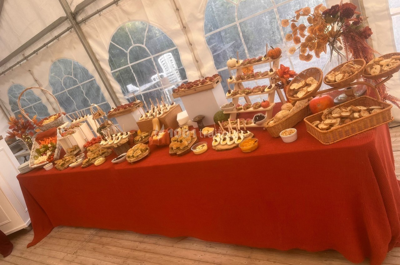 Buffet varié disposé sur une table rouge dans une tente, avec des plats salés et sucrés présentés sur plusieurs niveaux.