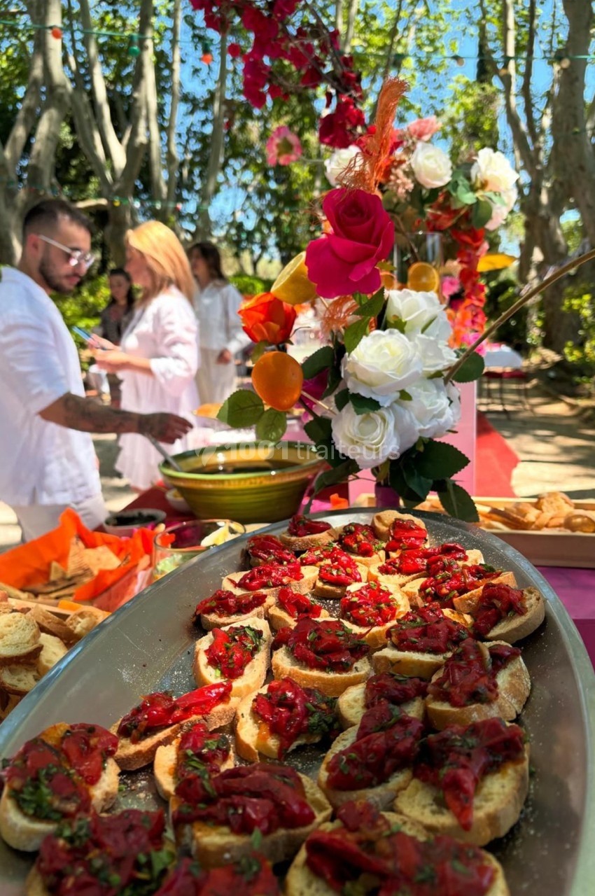 Plateau de bruschettas garnies de tomates et herbes, avec décor floral coloré en arrière-plan dans un cadre extérieur.
