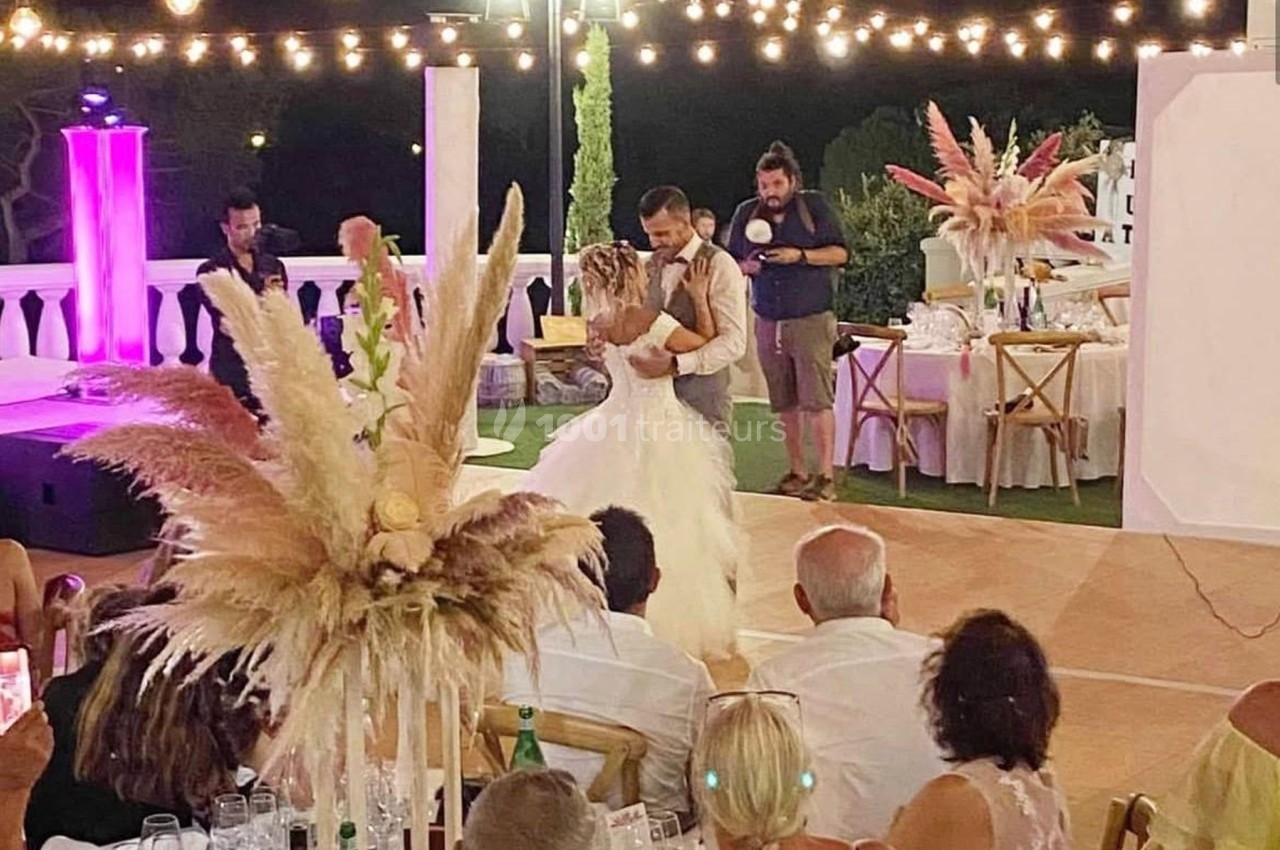 Un couple danse lors d'une réception de mariage en plein air, entouré d'invités et de décorations lumineuses.
