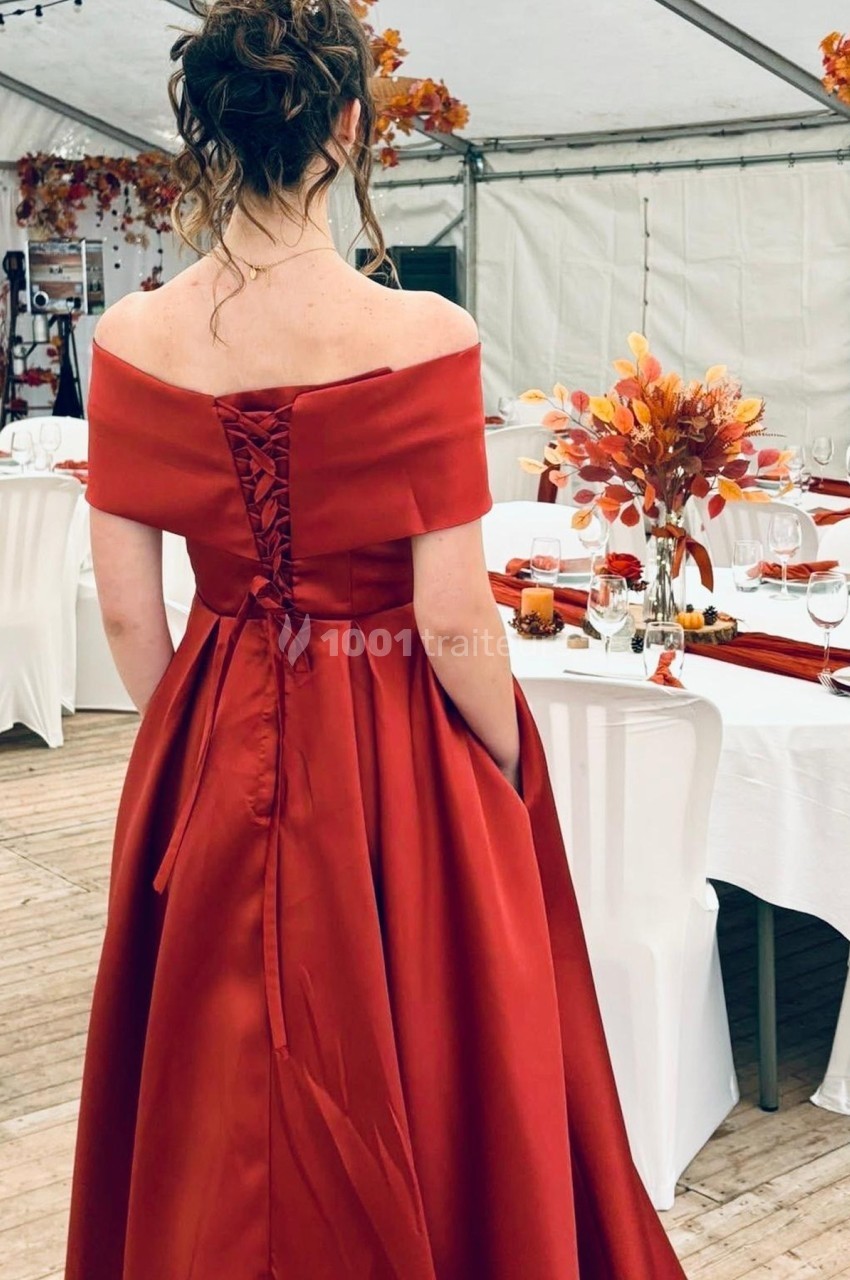 Femme en robe rouge élégante de dos dans une salle décorée pour un événement avec des tons automnaux.