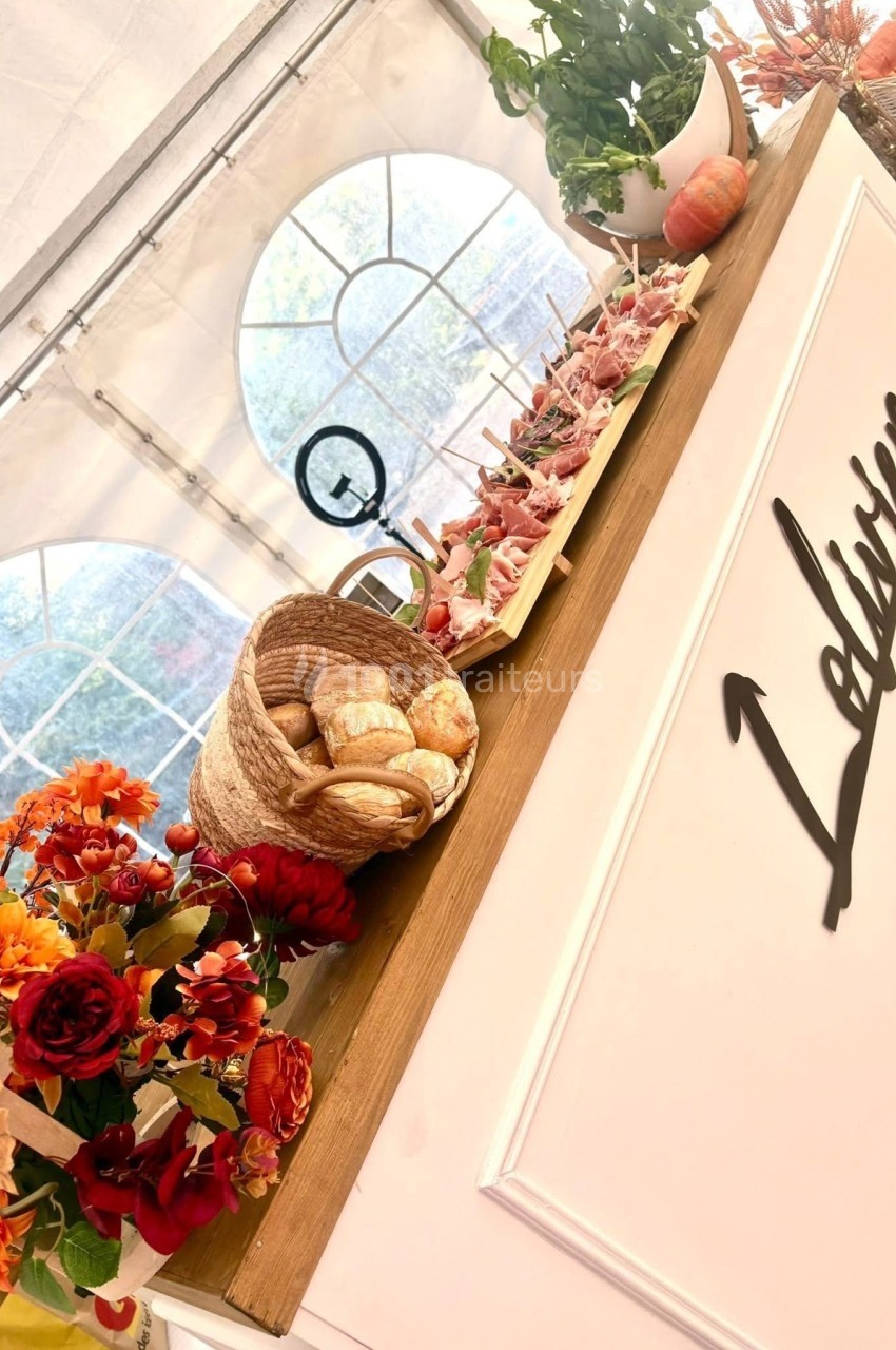 Plateau de charcuterie, panier de pain et décoration florale sur un comptoir en bois dans un espace lumineux.