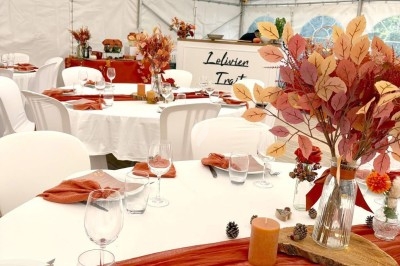Des invités assis à des tables décorées de fleurs et feuillages d'automne dans une grande tente lumineuse.