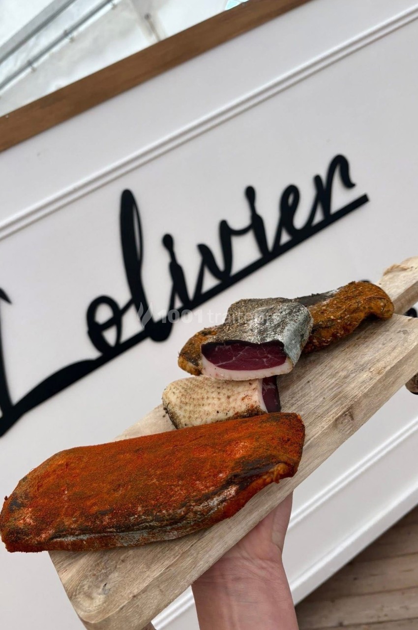 Planche en bois contenant des morceaux de poisson fumé et assaisonné, tenue devant un panneau blanc.